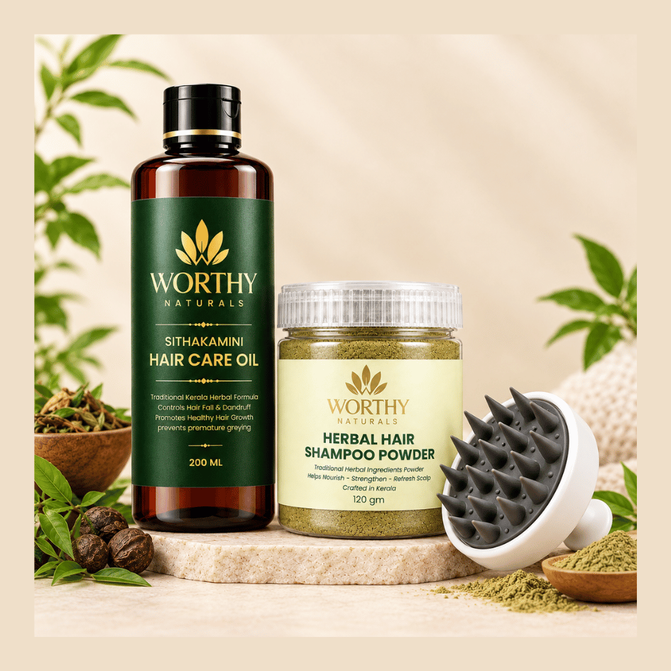 Three Worthy Naturals hair care products arranged on a stone slab with botanical props: a dark amber bottle of Sithakamini Hair Care Oil, a jar of Herbal Hair Shampoo Powder, and a white-and-gray scalp massager, all on a warm beige background.