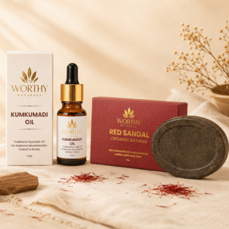 Worthy Naturals bath and oil set on a beige fabric surface, featuring Kumkumadi Oil in a dropper bottle, a white box, a red sandal organic bathing box, and a dark soap bar, styled with saffron threads and dried flowers.